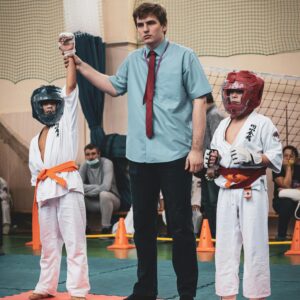 A referee declares the winner among two young karate participants in a sports event.