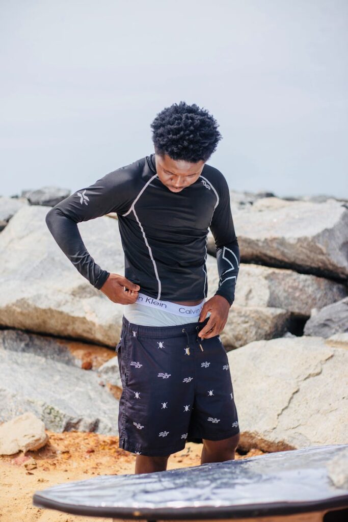 Surfer adjusting gear on rocky beach, ready for a day of adventure and relaxation.